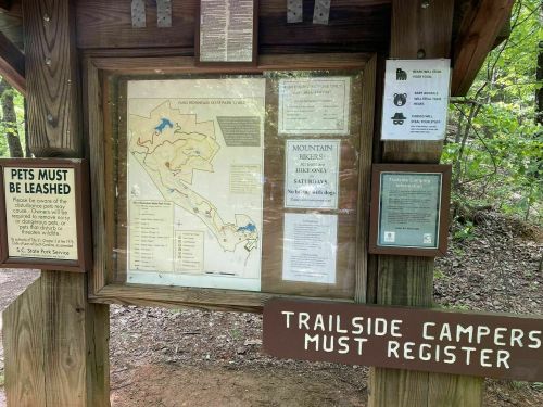 A wooden information board displaying a trail map and park rules in a forested area.