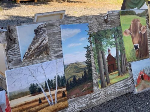 A rustic display of various landscape and animal paintings on a weathered wooden board.