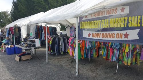Tents at a market displaying colorful clothing and accessories, with a sign for a t-shirt and hat sale.