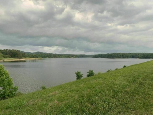 A serene lake surrounded by green hills and trees under a cloudy sky.