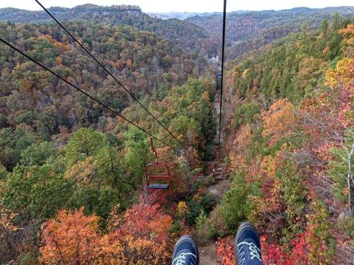 Aerial view from a chairlift over a colorful autumn forest with mountains in the background.