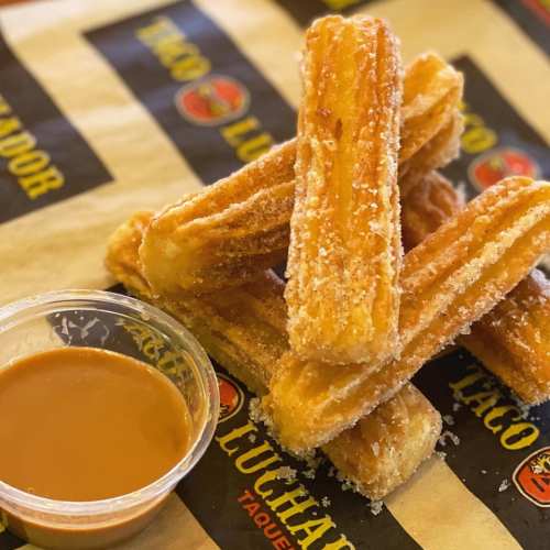 A stack of golden churros dusted with sugar, served with a small cup of caramel sauce on the side.
