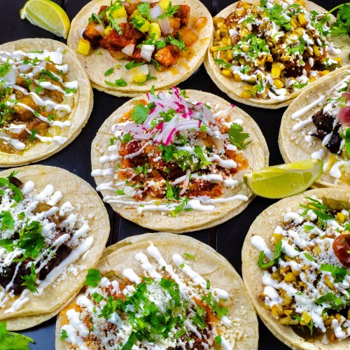 A colorful assortment of tacos topped with various ingredients, including meats, vegetables, and sauces, garnished with lime.