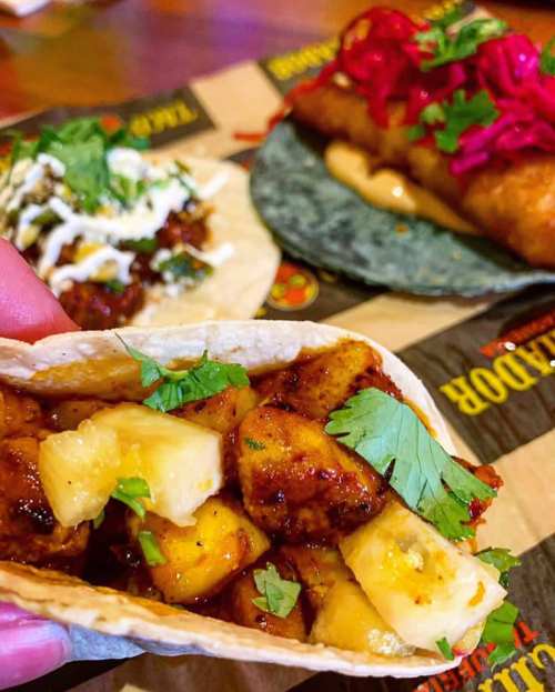 A hand holds a taco filled with diced pineapple and cilantro, with other tacos in the background.