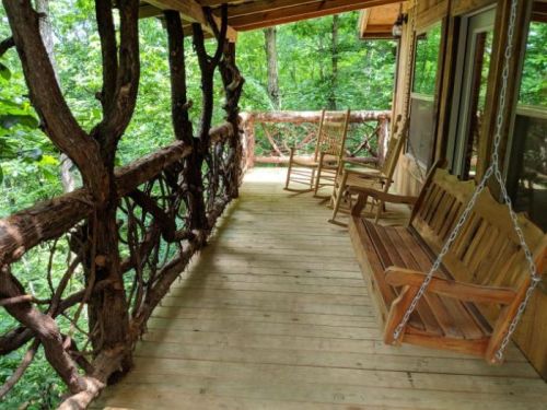 A wooden porch with rocking chairs, surrounded by lush green trees and a rustic railing.
