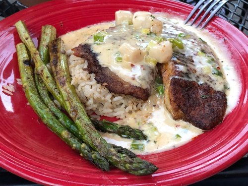 A red plate with grilled fish, creamy sauce, rice, and asparagus on the side.