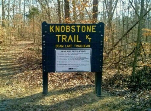 Sign for Knobstone Trail at Deam Lake Trailhead, with trail use regulations posted below. Surrounded by trees and leaves.