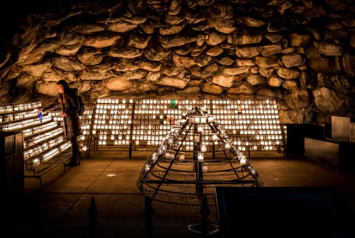 A person lights candles in a dimly lit stone chamber, surrounded by rows of glowing candles.