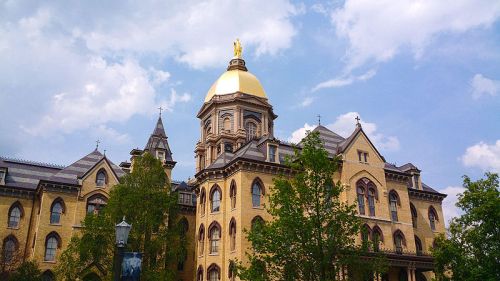 Historic building with a golden dome and statue, surrounded by trees under a partly cloudy sky.