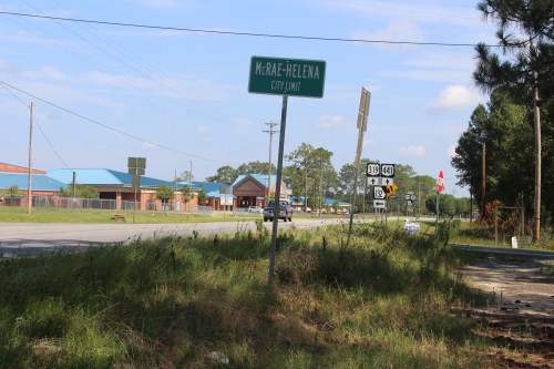 Sign indicating the city limit of McRae-Helena, with a view of the road and nearby buildings in the background.