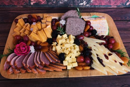 A beautifully arranged charcuterie board with various cheeses, meats, fruits, and garnishes on a wooden platter.