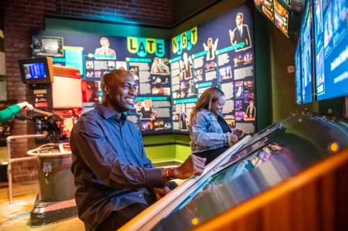A man and a woman interact with displays in a vibrant exhibit about late-night television.