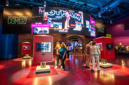 Visitors explore the National Comedy Center, surrounded by vibrant displays and interactive screens.