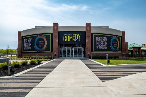 Exterior of the National Comedy Center, featuring large banners and a welcoming entrance on a sunny day.