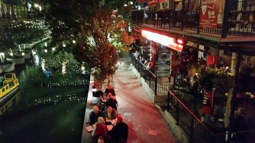 A lively canal-side scene at night, with diners enjoying meals and lights reflecting on the water.