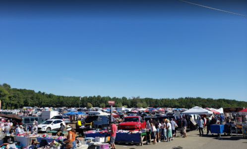 A bustling outdoor flea market with numerous vendors, shoppers, and colorful tents under a clear blue sky.