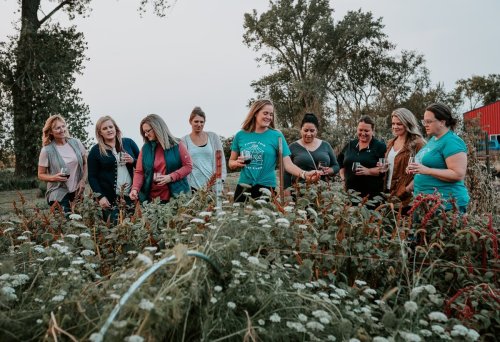 A group of women gathered in a field, engaging with plants and enjoying each other's company in a natural setting.