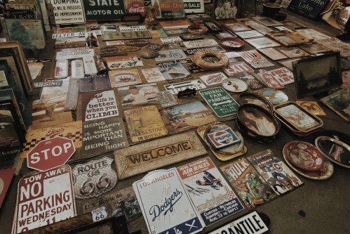 A collection of vintage signs and plates displayed on a floor, featuring various messages and designs.
