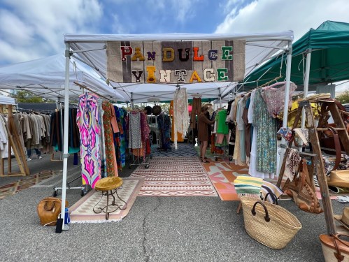 A vibrant vintage market stall with colorful clothing, accessories, and a sign reading "Pandulce Vintage" under a blue sky.
