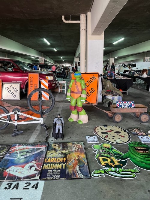A parking garage filled with vintage items, featuring a Ninja Turtle figure, posters, toys, and construction signs.