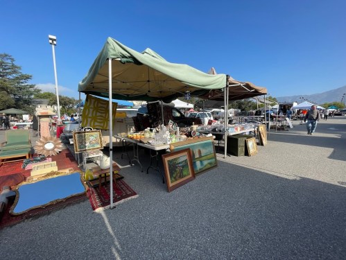 A vibrant outdoor market stall displaying various antiques and artworks under a canopy on a sunny day.