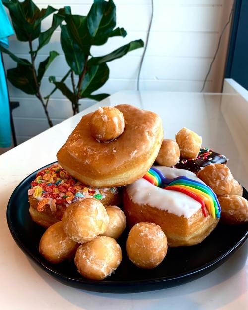 A black plate piled with various donuts, including frosted, glazed, and colorful cereal-topped varieties.