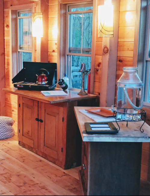 Cozy wooden interior with a kitchen area, featuring a kettle, grill, and decorative glass jar by the windows.