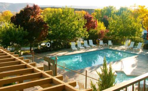 A serene pool area surrounded by colorful trees, with lounge chairs and a fence, under a clear blue sky.