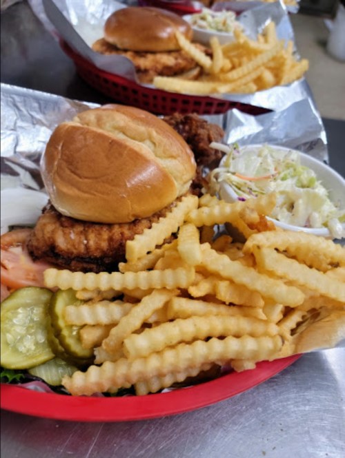 A fried chicken sandwich on a bun with crinkle-cut fries and a side of coleslaw in a red basket.