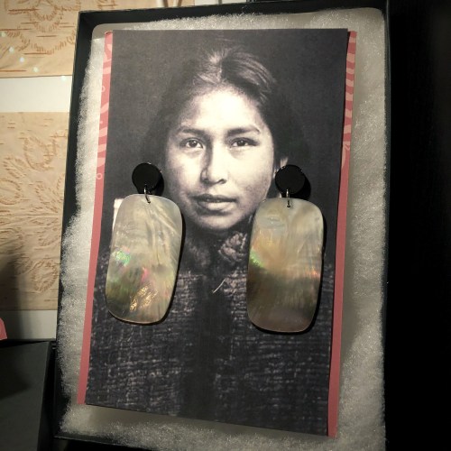 A vintage photo of a young woman with earrings displayed on a textured background.