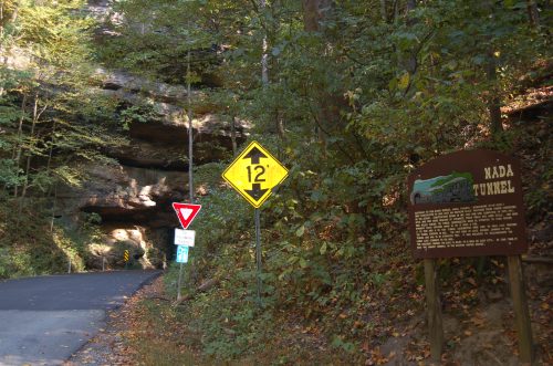 A road sign indicating the height limit for Nada Tunnel, surrounded by trees and rocky cliffs.