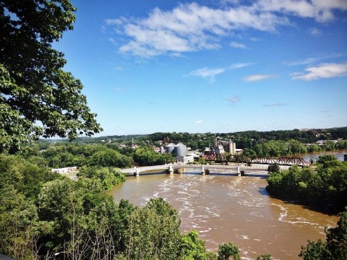 A scenic view of a river winding through a green landscape, with a town and blue sky in the background.