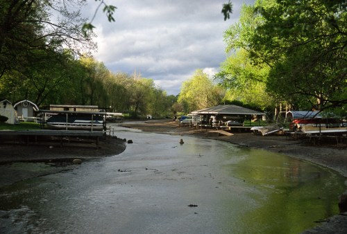 A serene river scene with green trees, a cloudy sky, and empty boat docks along the muddy banks.