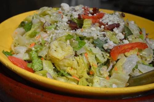 A vibrant salad with lettuce, tomatoes, cheese, and colorful vegetables served in a yellow bowl.