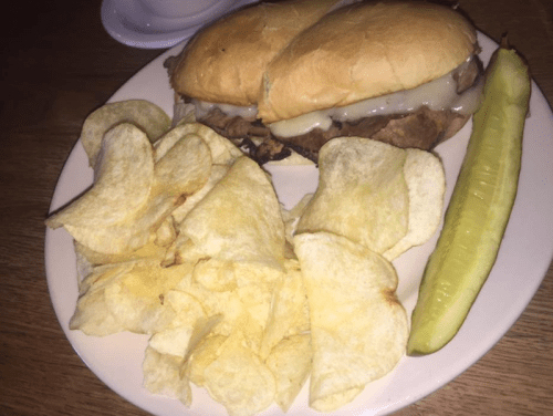A plate with two sandwiches, potato chips, and a pickle on the side.
