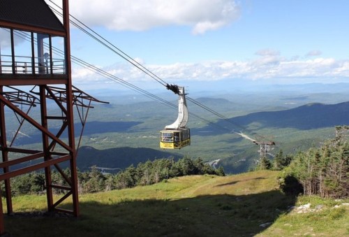 A cable car travels over lush green mountains under a blue sky with scattered clouds.