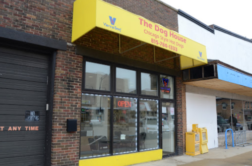Exterior of "The Dog House," a hot dog restaurant with a bright yellow awning and an "OPEN" sign.
