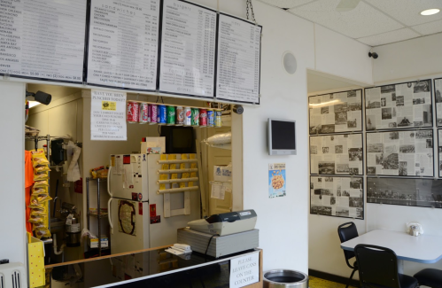 A small food counter with a menu board, drinks, and a wall covered in black-and-white photos.