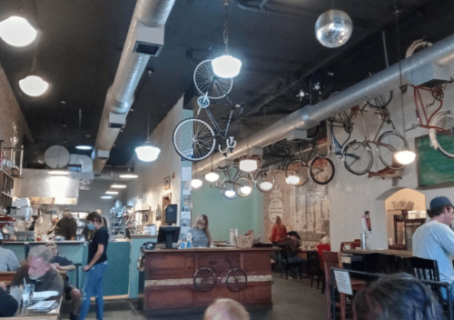 Interior of a trendy restaurant featuring hanging bicycles, a disco ball, and patrons dining at tables.