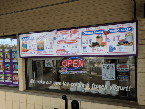 Menu board for a frozen yogurt shop featuring ice cream, shakes, and a neon "OPEN" sign in the window.