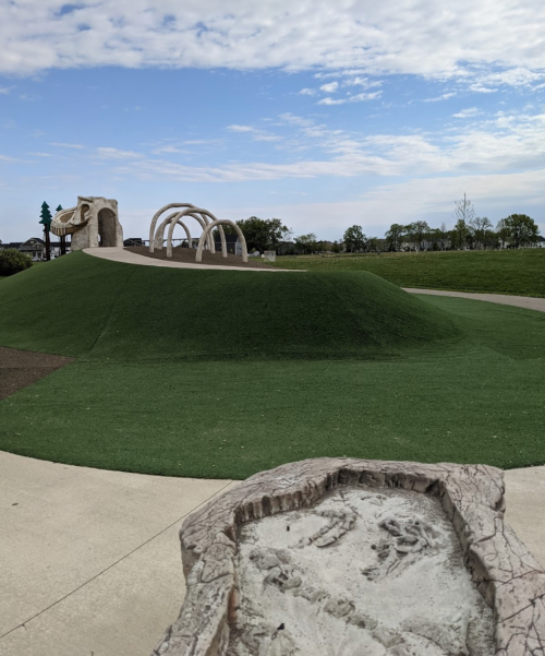 A grassy hill with abstract sculptures and pathways under a partly cloudy sky in a park setting.