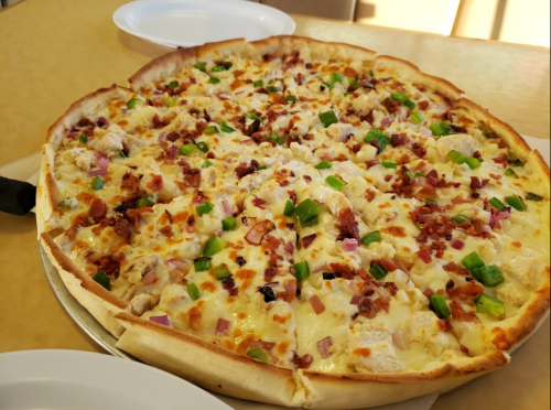A large pizza topped with chicken, bacon, green peppers, and onions on a golden crust, served on a table.