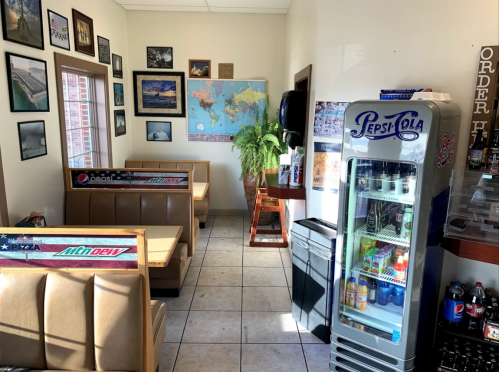 Cozy diner interior with booths, a world map, framed photos, and a Pepsi vending machine. Bright and inviting atmosphere.