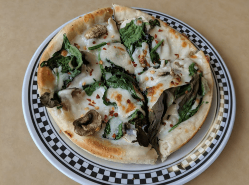 A slice of pizza topped with spinach, mushrooms, and melted cheese on a checkered plate.
