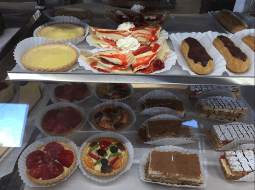 A display case filled with various desserts, including tarts, pastries, and layered cakes, all beautifully arranged.