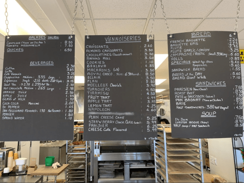 Menu boards displaying various food items, including salads, pastries, beverages, and sandwiches, with prices listed.