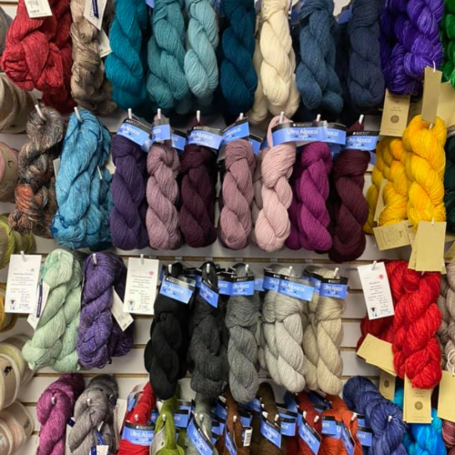 A colorful display of various yarn skeins arranged neatly on a wall, showcasing a range of textures and shades.