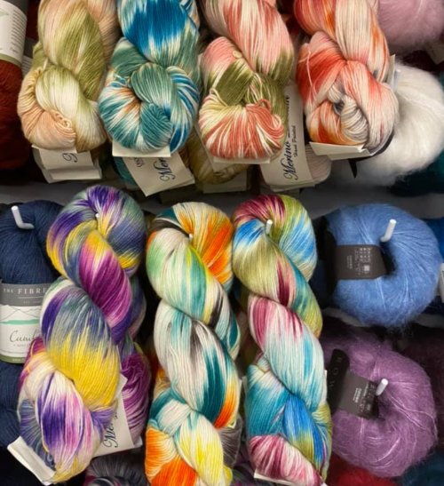 A colorful display of various yarn skeins in vibrant hues, arranged neatly on shelves.