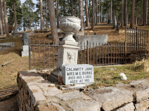 Gravestone of Calamity Jane, Mrs. M.E. Burke, died August 1, 1903, aged 47 years, in a wooded cemetery.