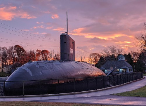 A decommissioned submarine on display, surrounded by a fence, with a colorful sunset in the background.